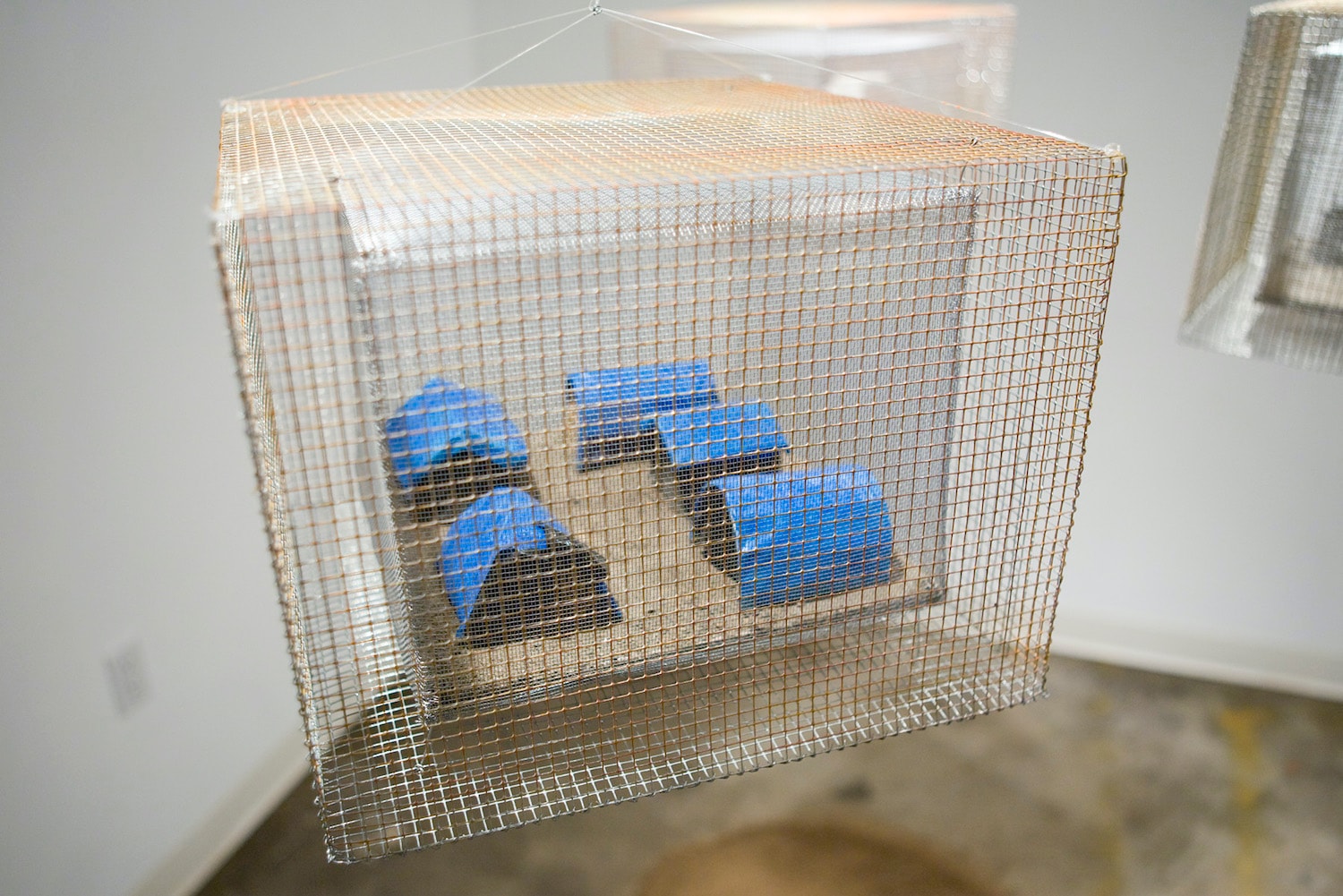Congo camp mixed-media installation enclosed in wire mesh with blue forms