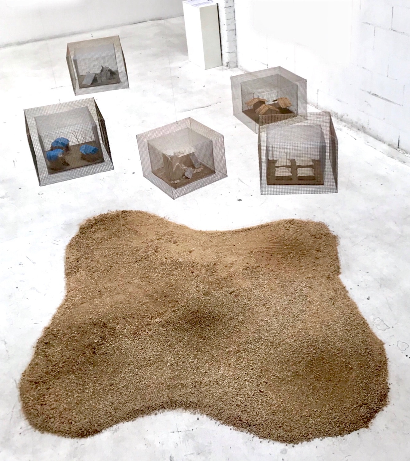 Far from Home installation at Artspace 1616 with wire enclosures arranged around a bed of granular material